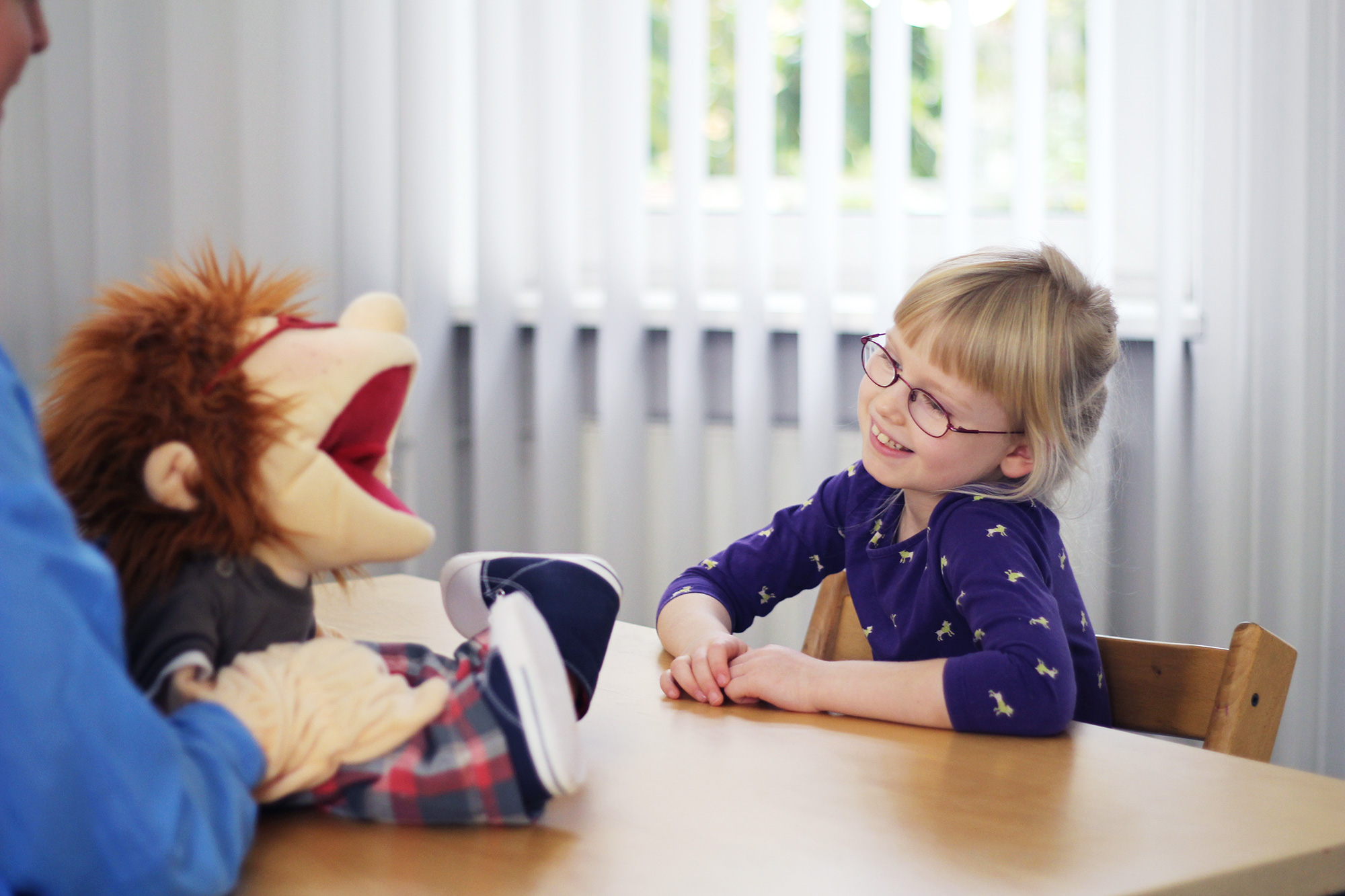 Logopädische Therapie mit Handpuppe: lachendes Mädchen mit Brille in der Logopädie-Praxis in Berlin-Spandau